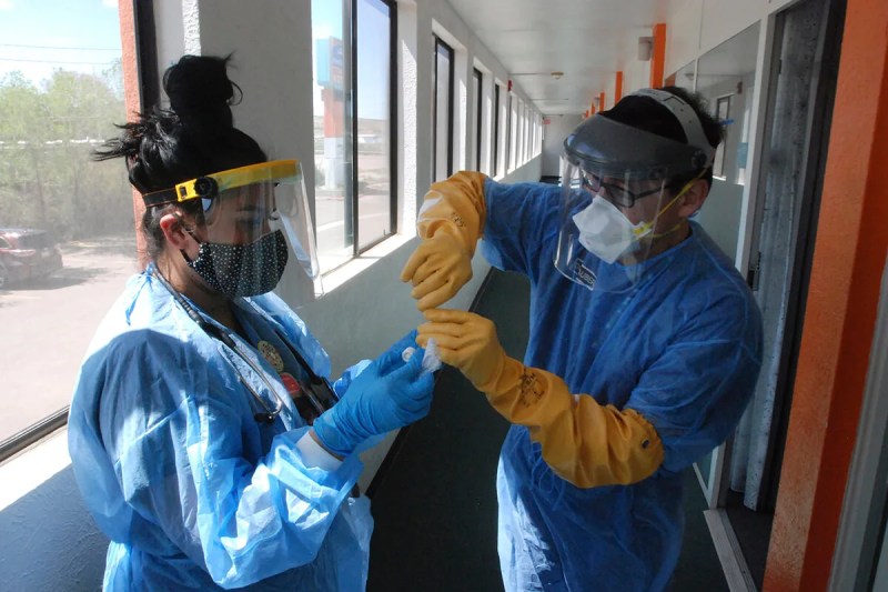 two healthcare workers dressed in smocks and masks test a coronavirus test sample