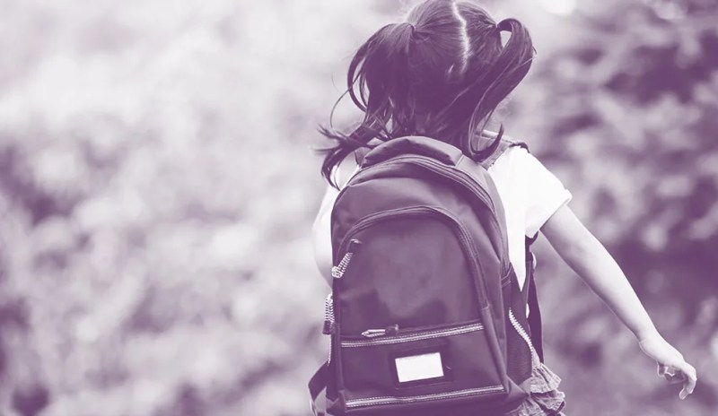 child with pigtails running with backpack on