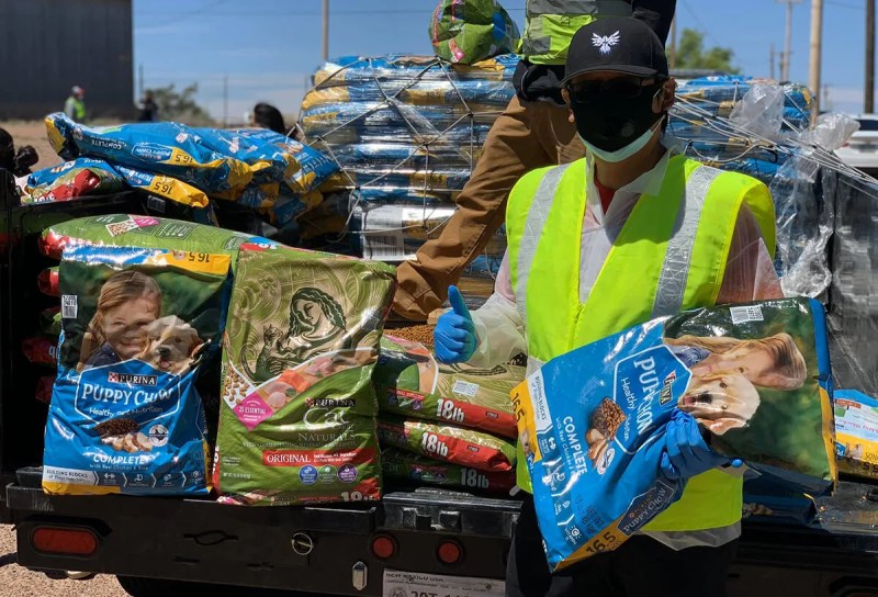 man in safety vest and mask holding pet food and making thumbs up sign