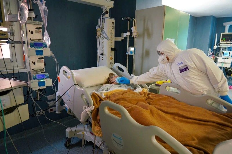 medical workers in protective suit places hand on patient in ICE bed