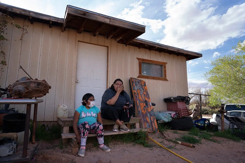 child in mask and woman sitting in front of a house