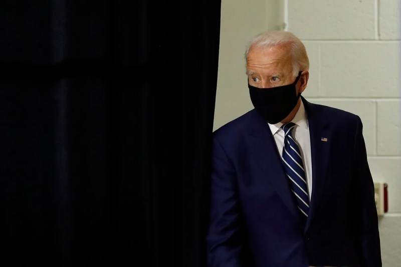 Joe Biden walking out from a stage curtain wearing a face mask