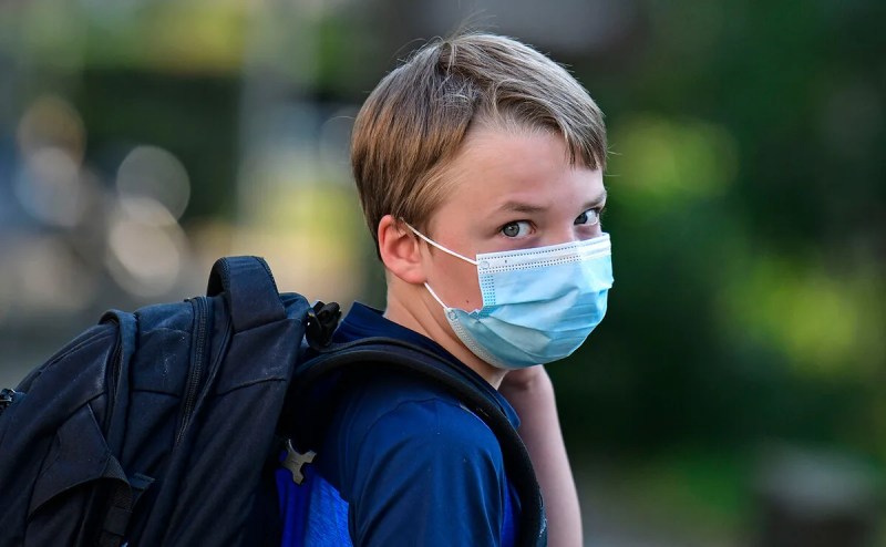 child looking at camera wearing face mask and backpack