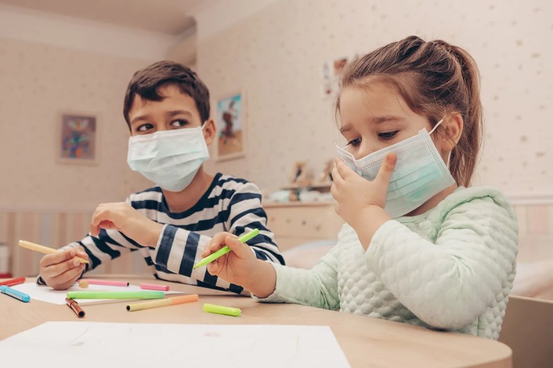 two children wearing face masks sitting at a table drawing