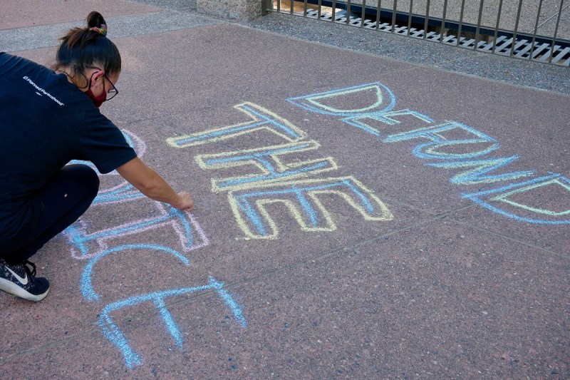woman writes "defund the police" in chalk on asphalt