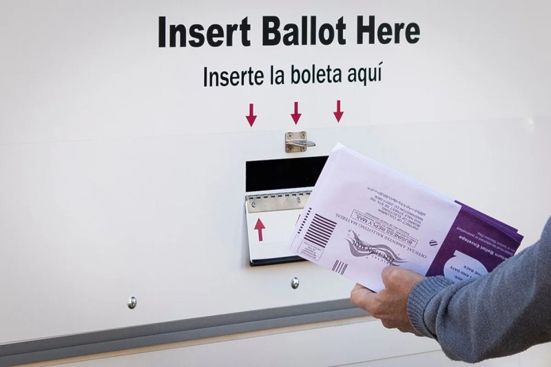 hand holding early ballots up to ballot drop box slot