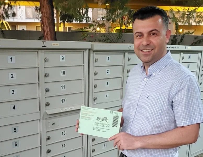 Bilal Alobaidi holding his ballot in front of mailboxes