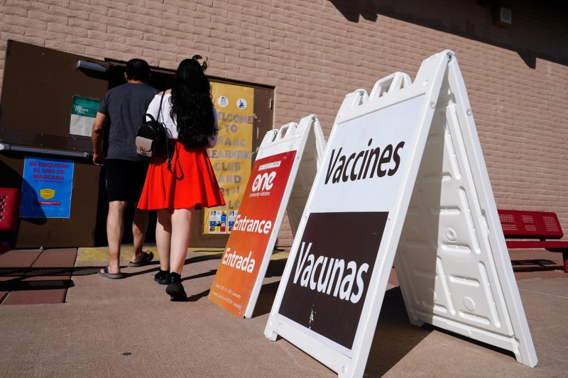 people filing into a building with "vaccines" sign out front