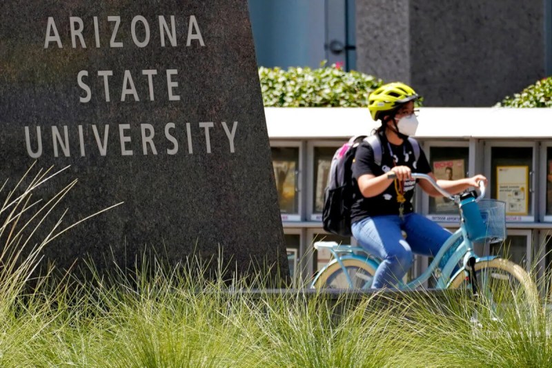 masked student bikes past ASU sign