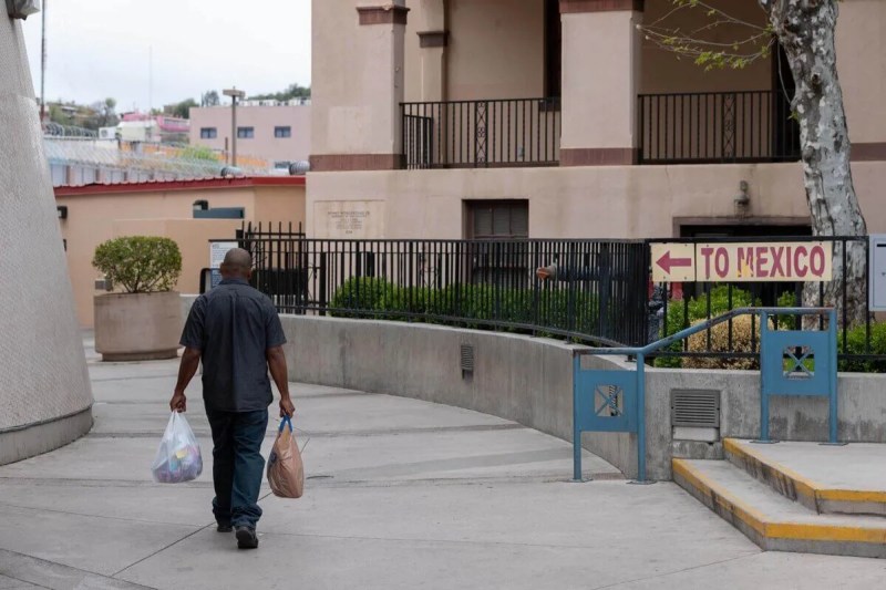 A person holding bags walking toward a "to Mexico" sign