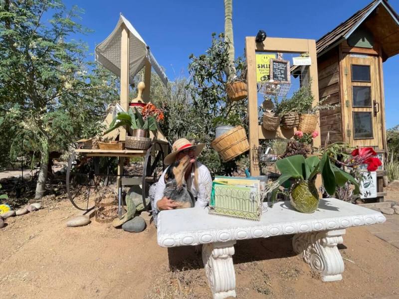 woman and her dog pose in front of outdoor furniture filled with plants