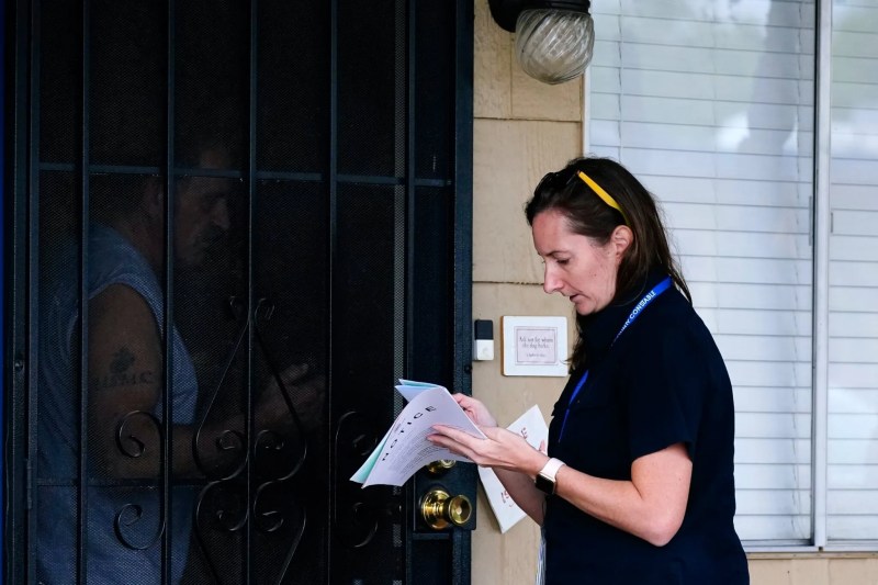 woman looking at packet of papers while a man stands inside his doorway