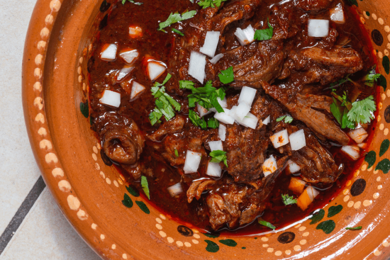 A large bowl of birria with onions.