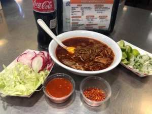 A bowl of birria with salsa and veggies on the side.