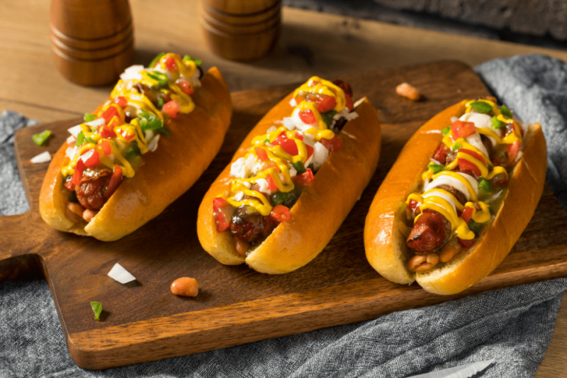 Three Sonoran hot dogs on a wooden cutting board.