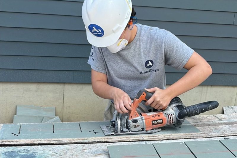 woman in AmeriCorps outfit using power saw