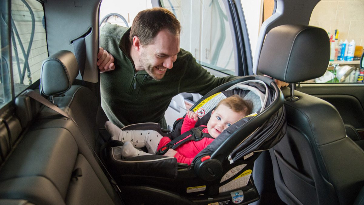 Man smiling at baby buckled into car seat.
