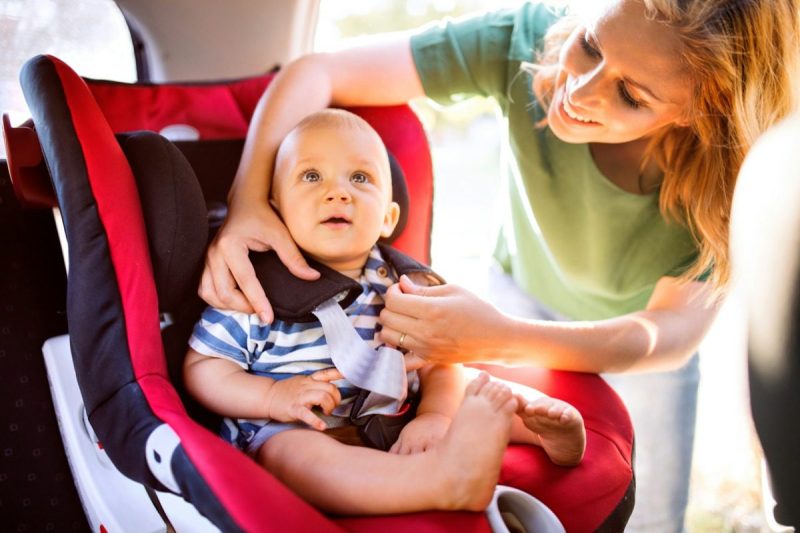 Woman smiling while buckling her baby into a car seat.