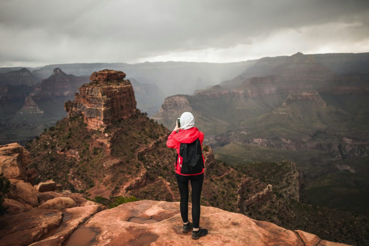Woman in a red jacket and hoodie taking a picture at an Arizona state park.