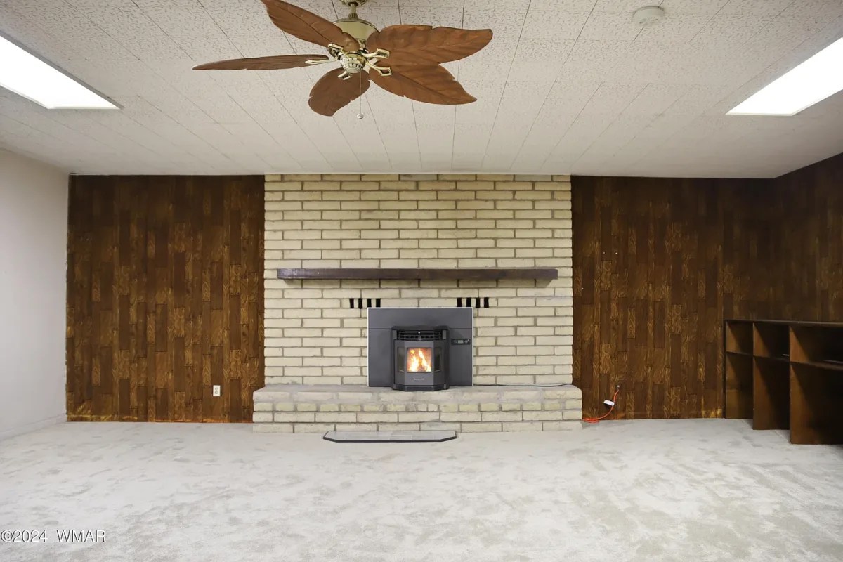 empty room with wood walls, carpeted floor, brick fireplace, and brown ceiling fan