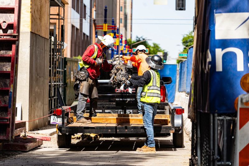 Construction workers take items and materials off a cable and load them on onto a pickup truck