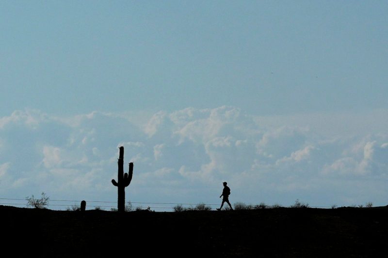 storm clouds in sky as silhouette of hiker walks through