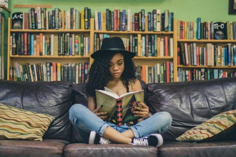 woman reading a book on a couch with bookshelves behind her