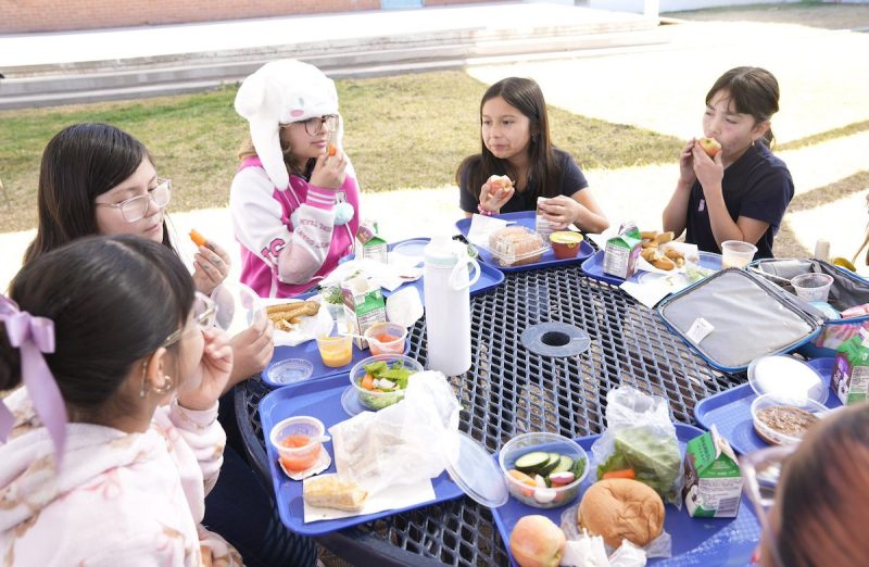 fourth grade students sitting around table eating lunches that include fresh produce
