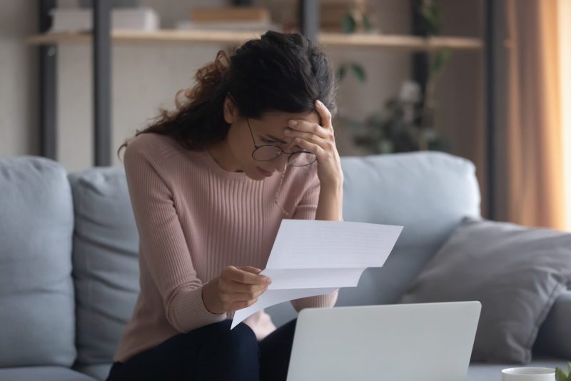 woman sitting on couch looking at piece of paper and looking stressed