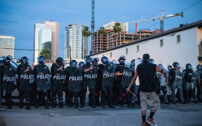 protester standing in front of line of police officers wearing riot gear