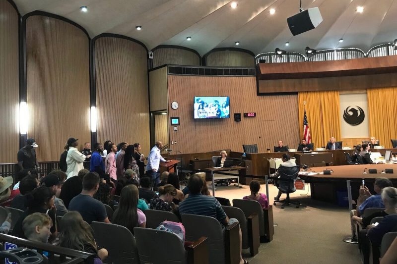 group of people standing behind podium and man speaking into mic in front of City Council
