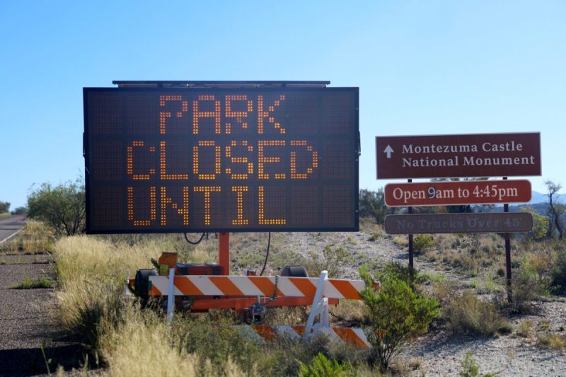 A sign that says "park closed until" next to a sign for Montezuma Castle National Monument