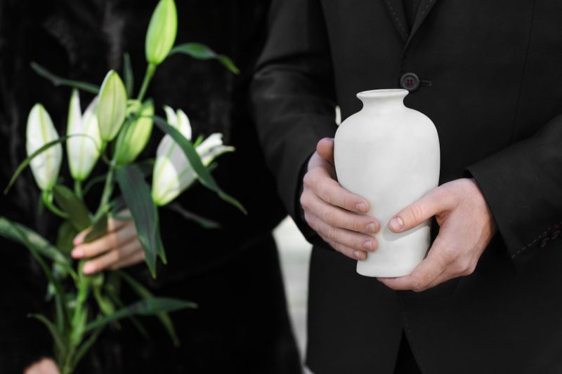 close-up of two pairs of hands holding flowers and a white urn