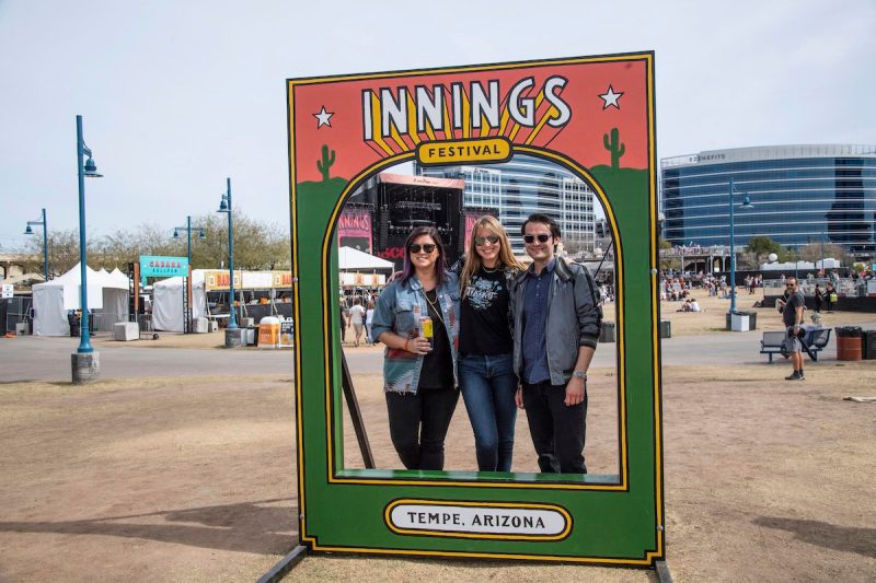 people posing inside of a stand that says Innings Festival Tempe Arizona