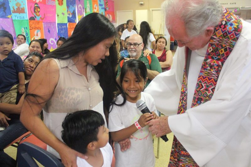 a woman standing with two kids as reverend holds mic up to child