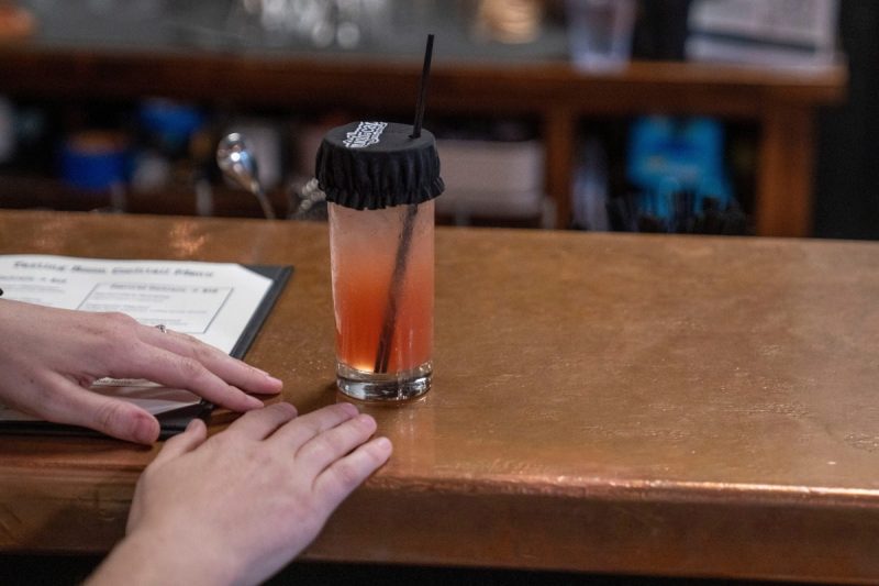 drink sitting on a bar with a black cover over the top with straw poking through hole