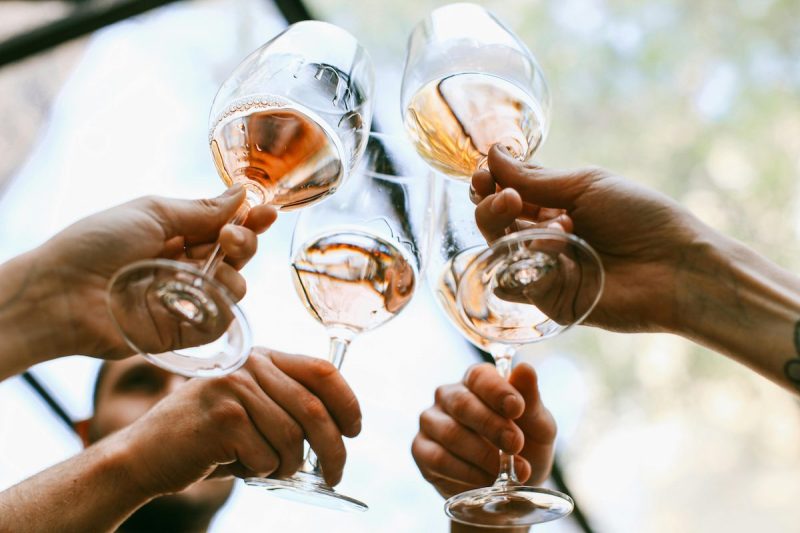 four hands holding wine glasses toasting them together