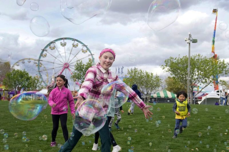 three kids running around at a fair chasing bubbles