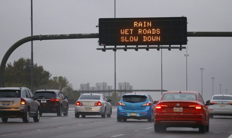 cars on a freeway with an overhead sign saying rain wet roads slow down