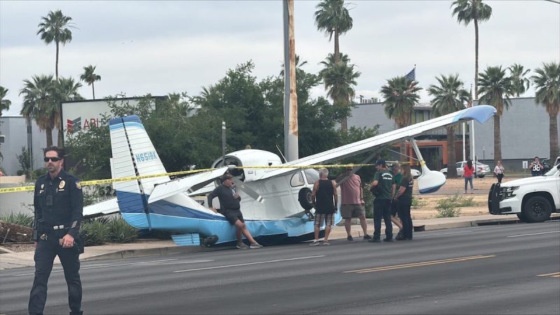 a small plane landed on a road, surrounded by by police tape, people, and police officers